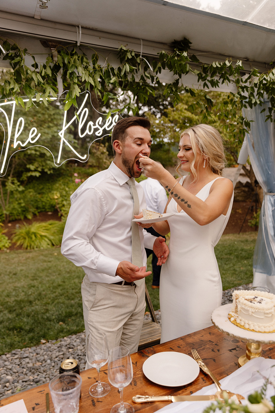 The bride and groom feeding each other cake during the cake cutting surrounded by lush greenery